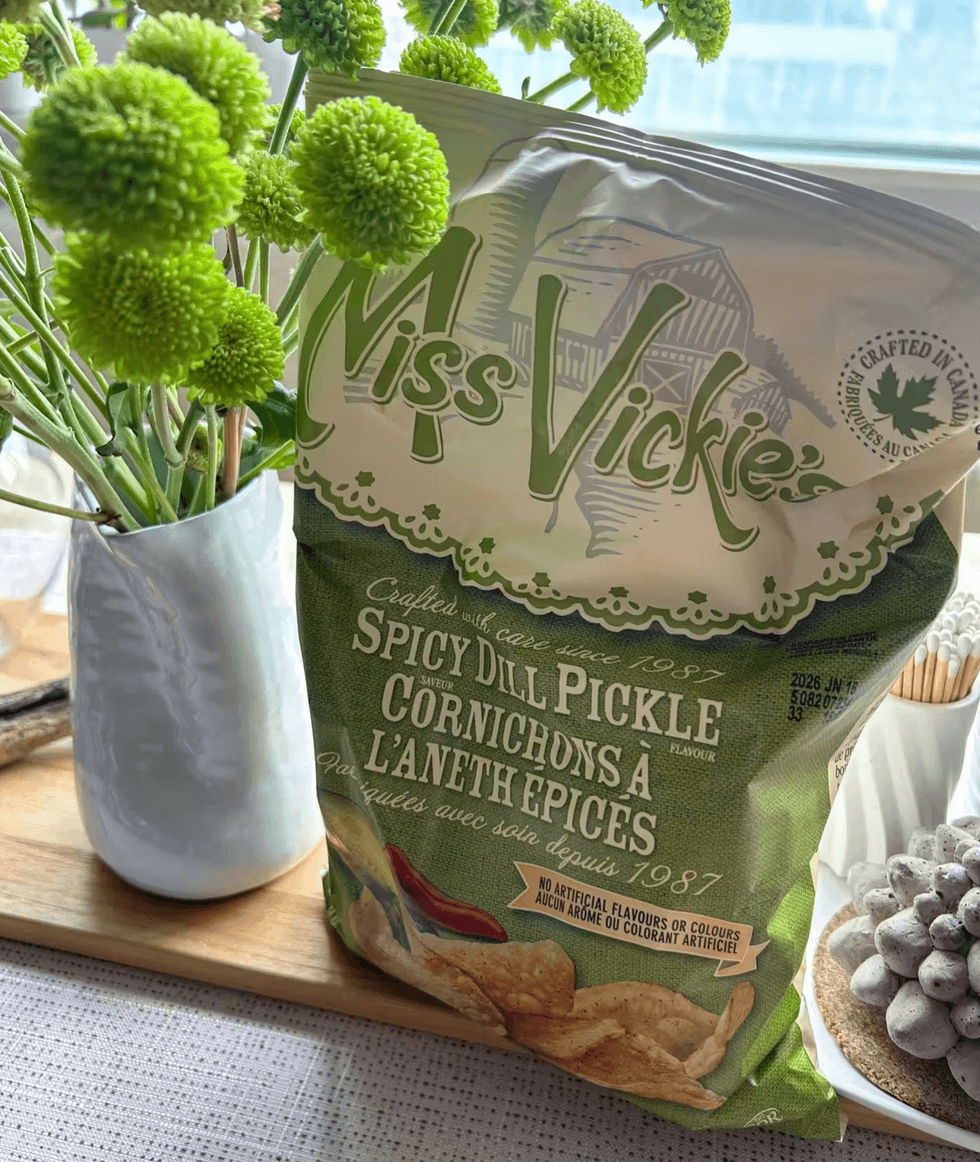 A bag of Miss Vickie's spicy dill pickle chips on a kitchen counter next to fresh flowers.