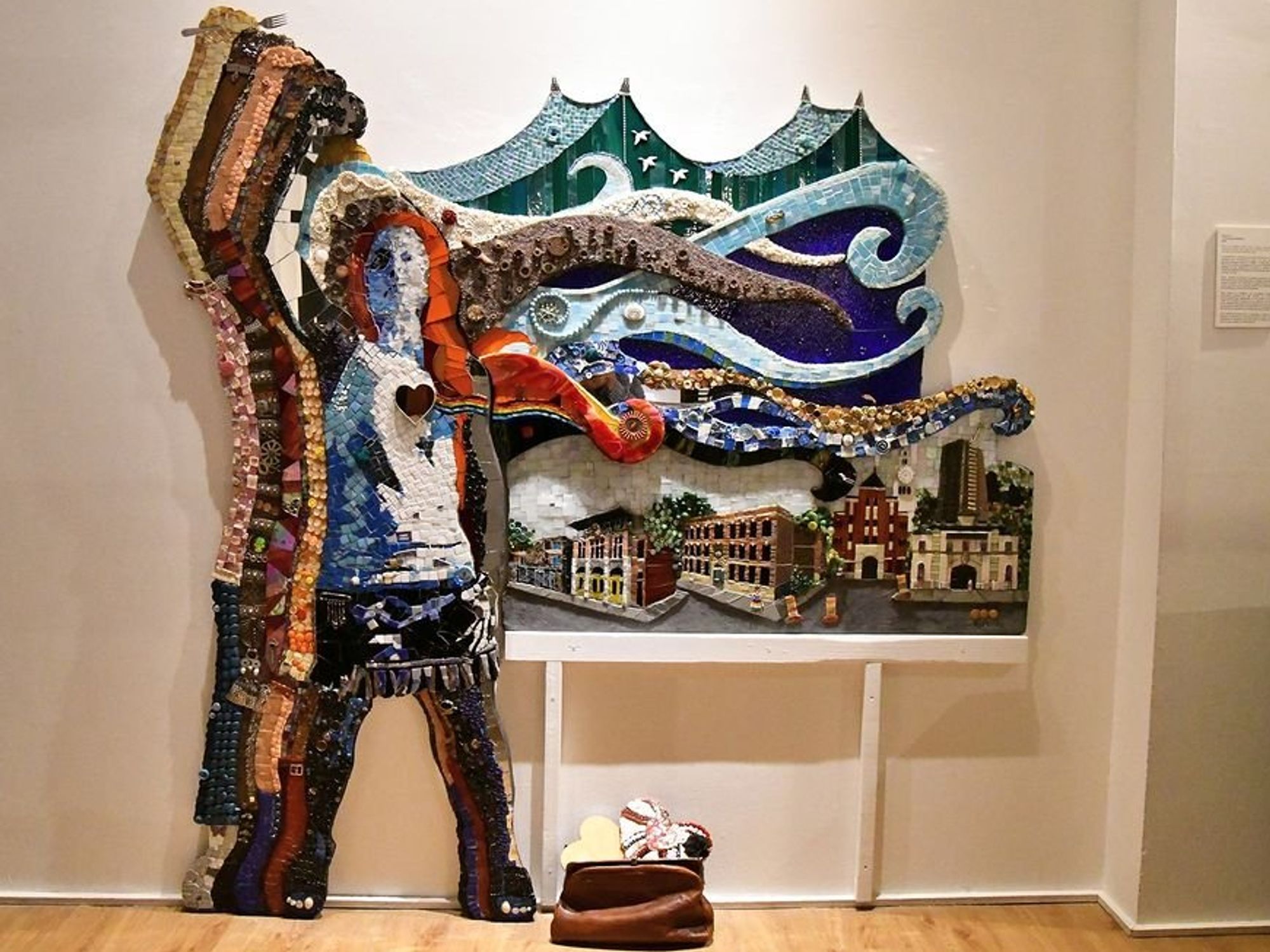 A bas-relief mosaic portraying a woman with a raised fist, her heart, and limbs reflecting the diversity of women activists over five decades, while her hair transforms into Montreal's urban landscape, symbolizing the community's struggles and triumphs.