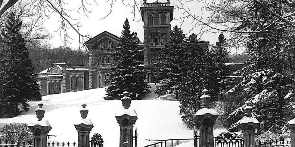 A black-and-white photo shows an old building amongst trees in the snow.