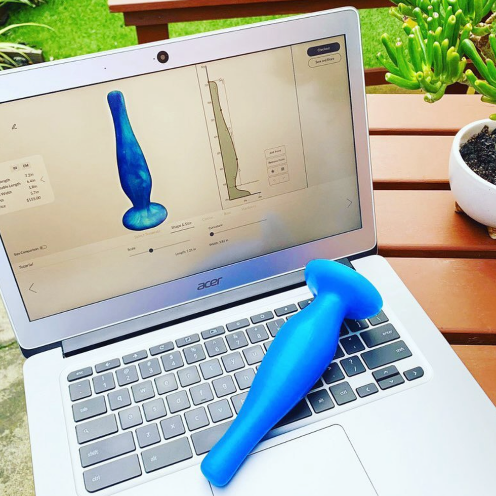 A blue butt plug on a laptop keyboard in front of a screen showing the design in the Freely custom builder.