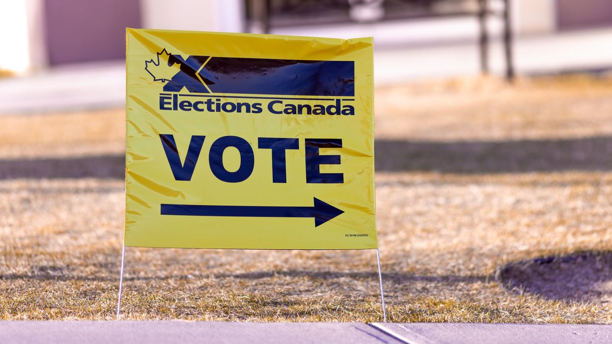 A bright yellow Elections Canada sign with the word "VOTE" and an arrow pointing to the right, placed on a grassy area near a sidewalk.