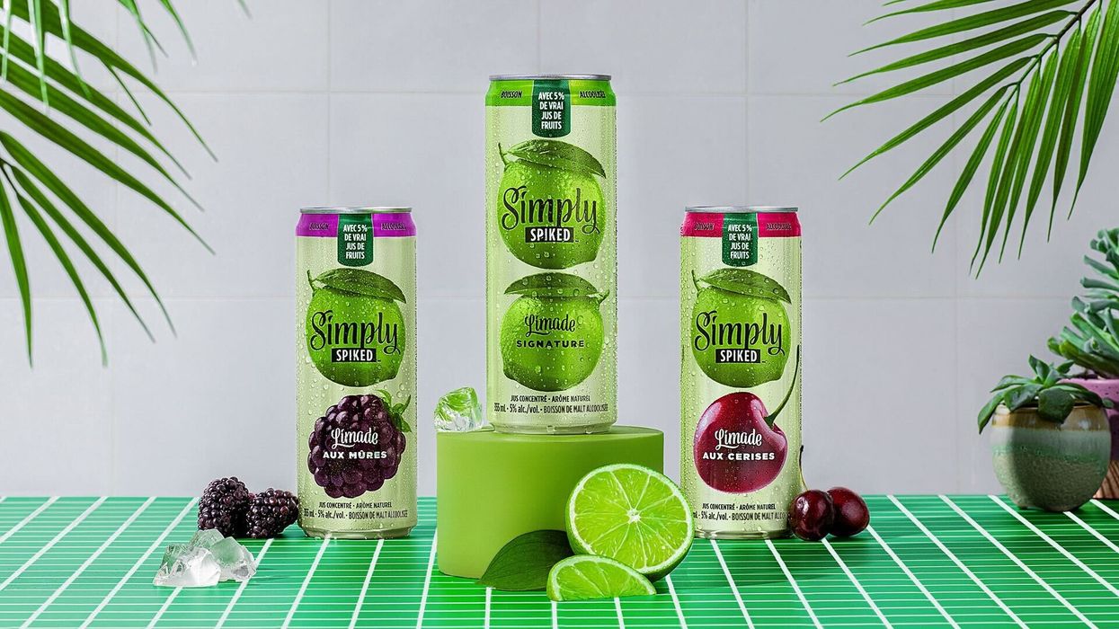 A can of each of the three flavours of Simply Spiked Limeade arranged on a green tiled table with fresh lime, cherry and blackberries.
