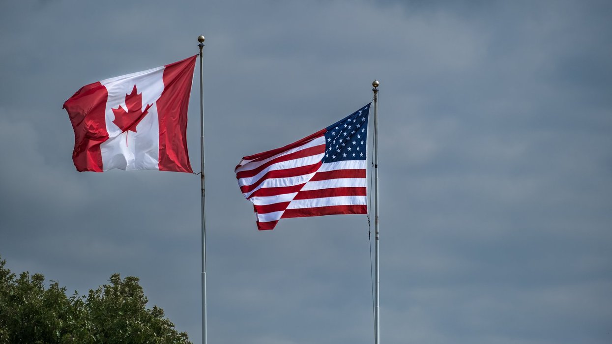A Canadian flag flies beside an American flag, dark grey skies are visible in the background.