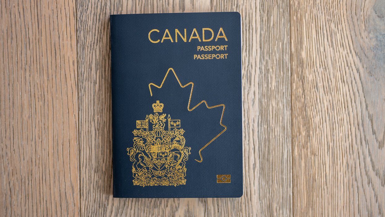 A Canadian passport with a navy blue cover lies flat on a wooden surface.