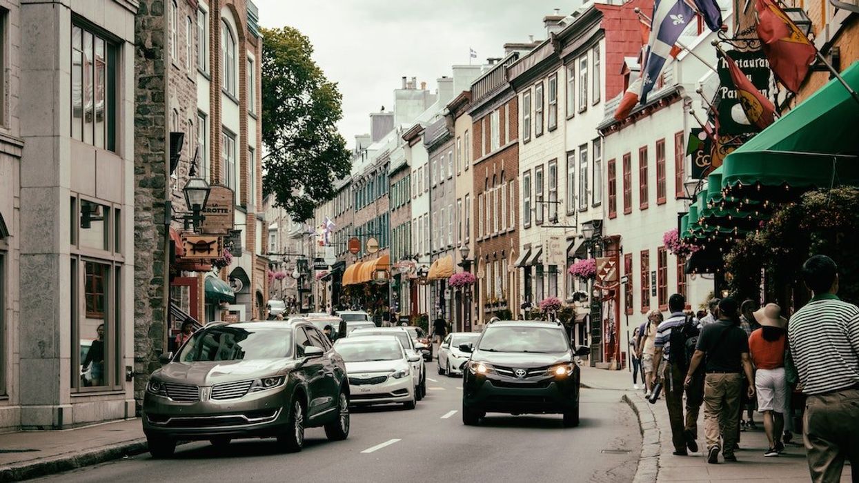 A car comes down a street in Quebec City while pedestrians walk the sidewalks.