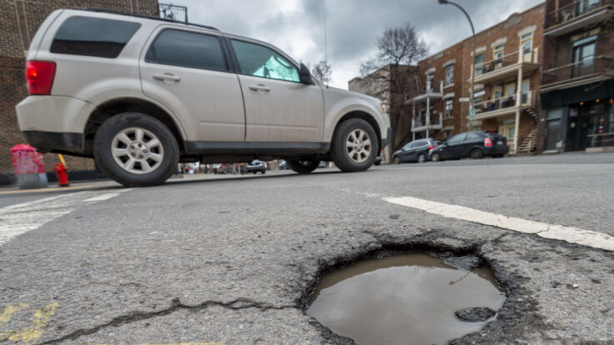 A car drives past a large pothole filled with water on a Montreal street.