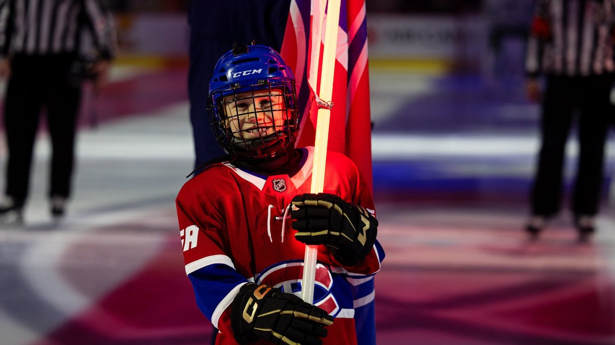 A child wearing a Habs jersey holding a Canadiens flag with a glowing pole on the ice at Centre Bell.