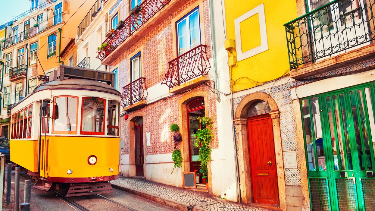 A classic yellow tram travels along a narrow cobblestone street in Lisbon, Portugal.