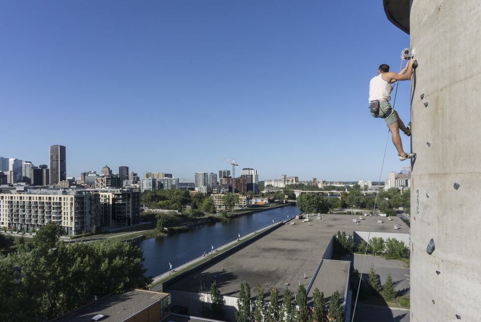 A climber looks out at the city while scaling the exterior of a sugar silo.
