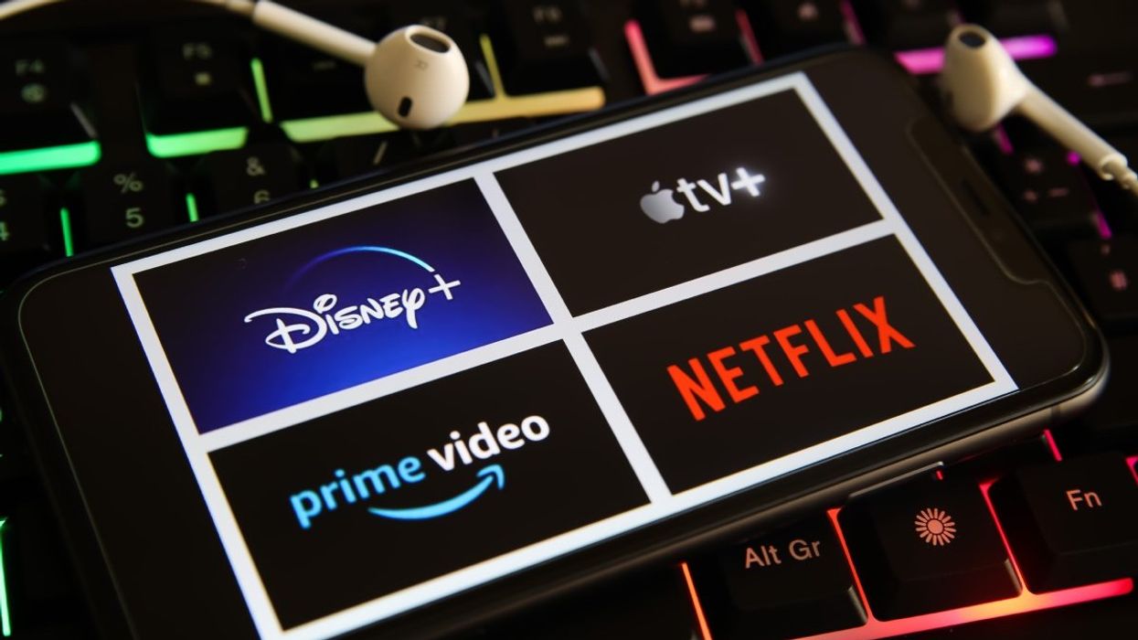 A closeup of mobile phone screen with logo lettering of various tv movie streaming services on laptop keyboard.