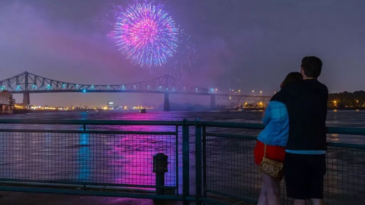 A couple at Clock Tower Beach watches fireworks light up the surface of the Saint Lawrence River.