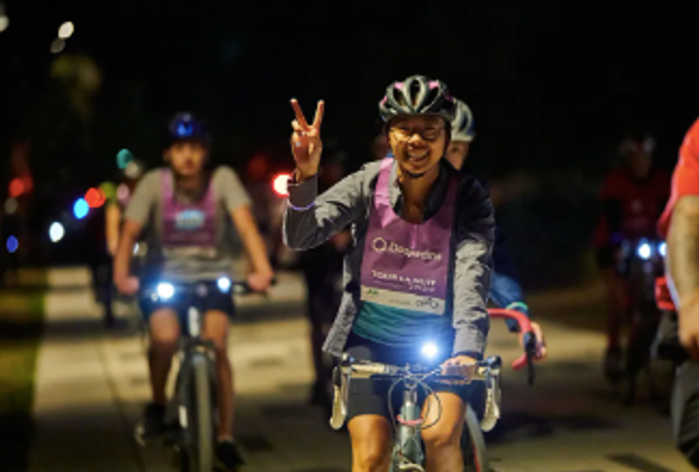 A cyclist throws up a peace hand sign while on a bike.