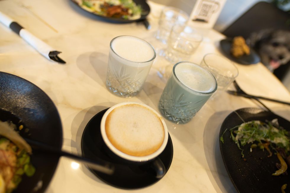 A foamed coffee drink in a black cup and saucer, along with two pastel-hued drinks in glasses.
