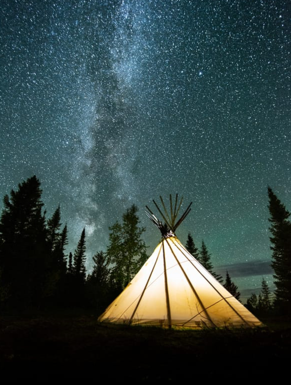 A glowing tent surrounded by stars at Nibiischii National Park.