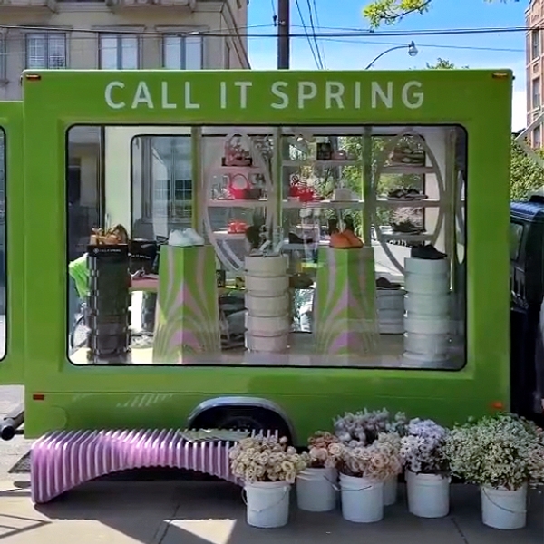 A green truck parked on a street with buckets of flowers out front.