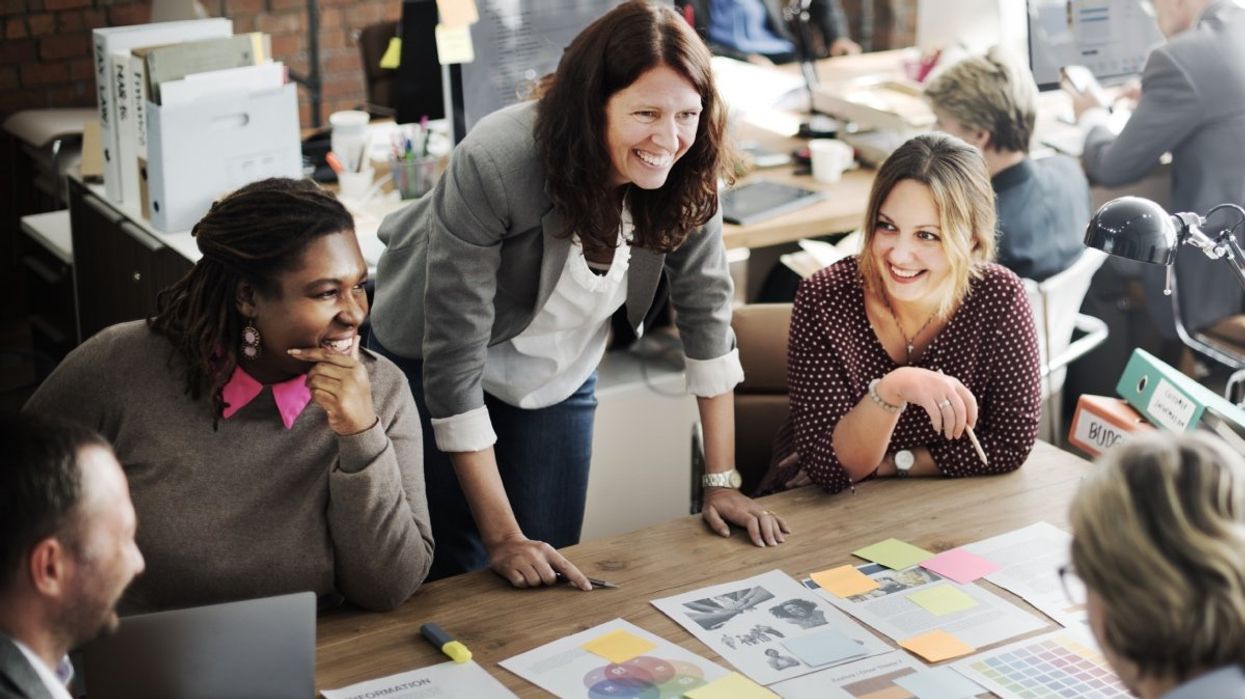 A group of people sitting at a large office desk discussing work-related plans.