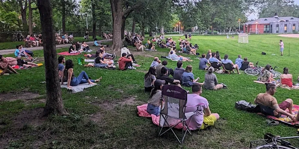 A group of people sitting in a Montreal park watching a free comedy show.
