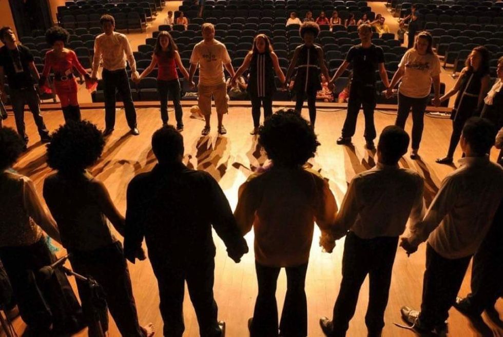 A group of people standing on a stage in a circle all holding hands.