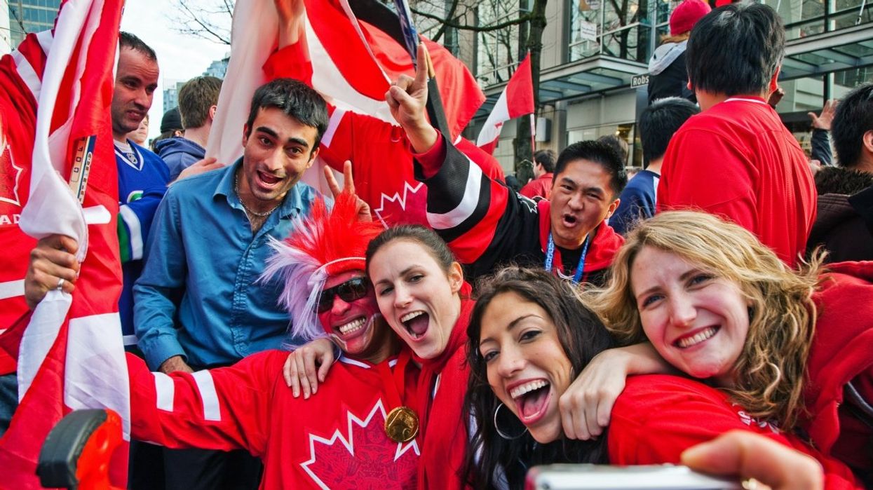 A group of people wearing Canadian hockey jerseys and holding Canadian flags while all taking a photo together smiling.