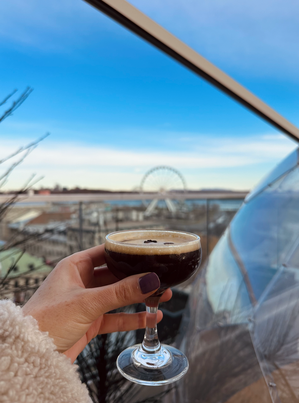 A hand holds an expresso martini with panoramic Montreal views in the background.