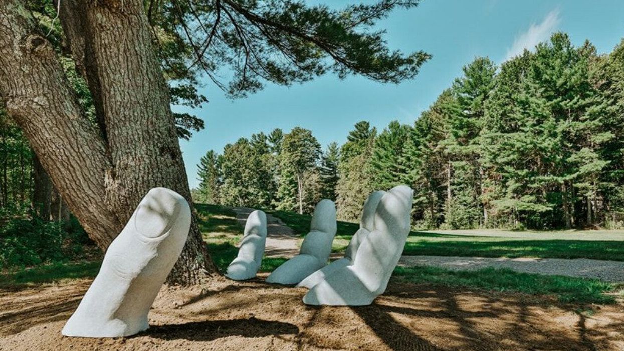 A hand sculpture sticking out of the ground around the base of a tree in the forest.