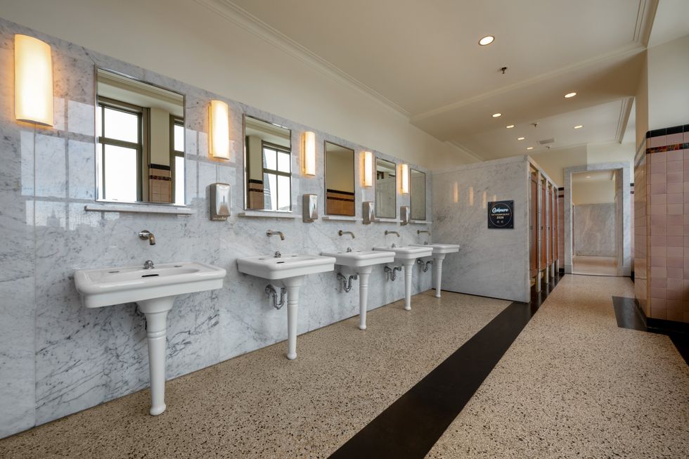 A large, elegant restaurant bathroom with white basins and marble walls.