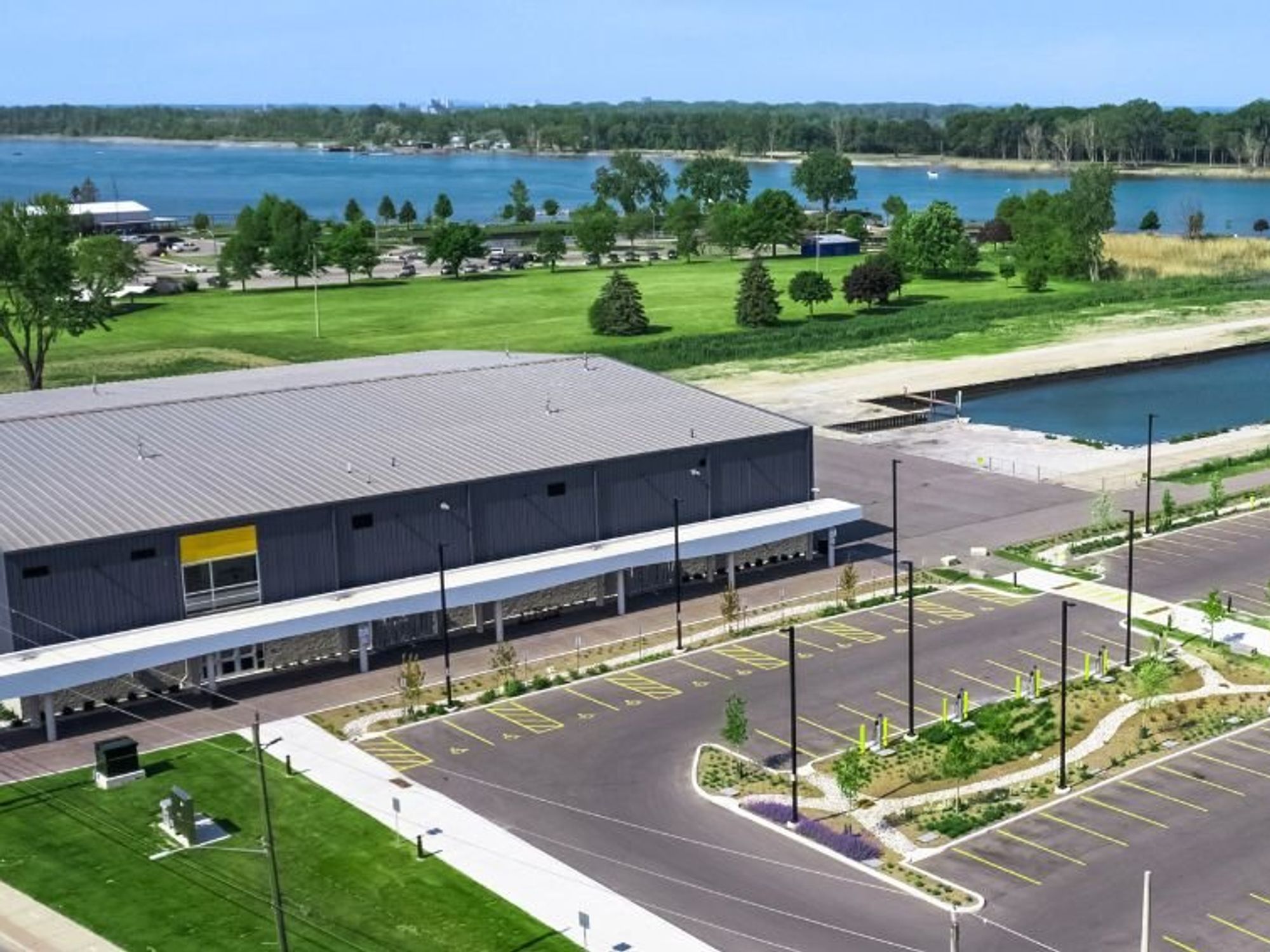 A large grey building and parking lot surrounded by greenery with a waterway in the background.