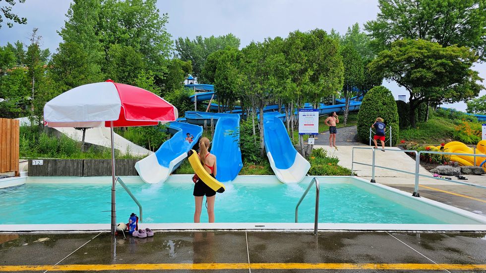 A lifeguard stands at the base of three water slides.