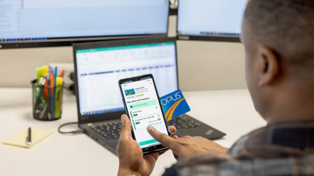A man sitting at a desk, seemingly at work, recharges his OPUS card using his phone.