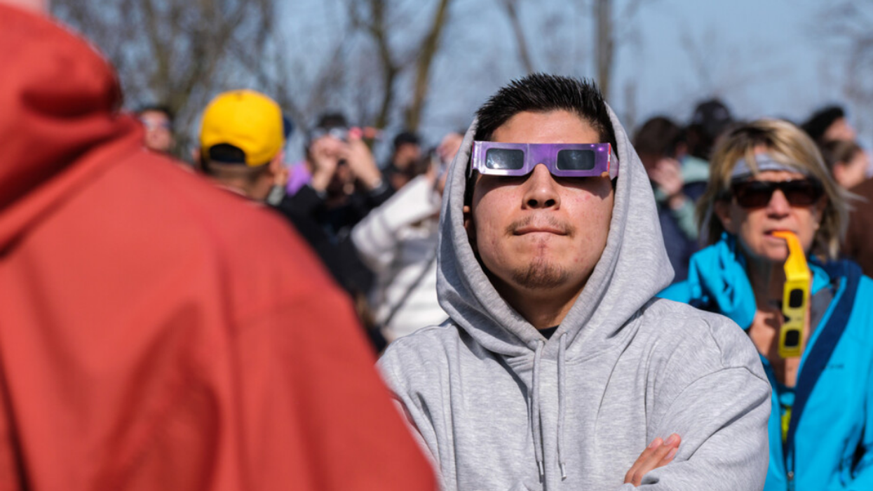 A man wearing eclipse glasses looks up to watch 2024 total solar eclipse amongst a crowd in Montreal.