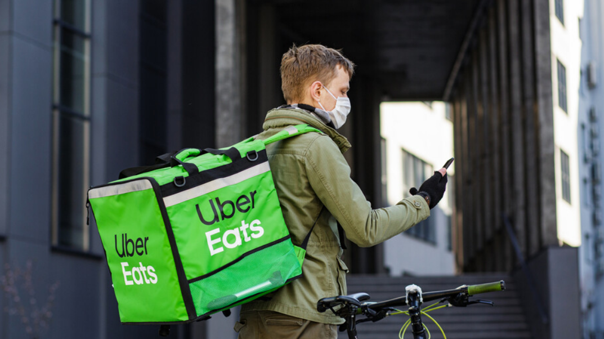 A masked Uber Eats delivery biker checks their phone.