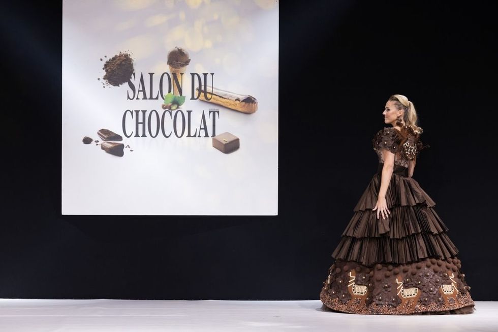 A model in a chocolate princess dress in front of a "Salon du Chocolat."
