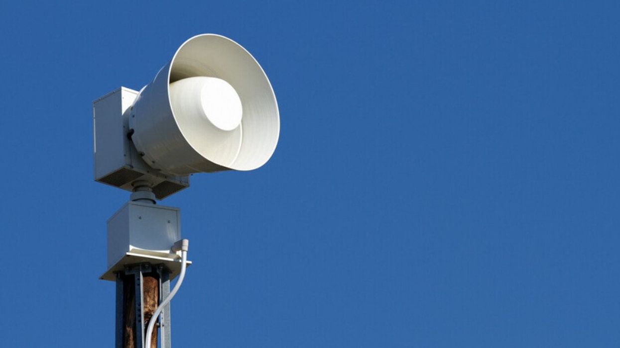 A modern public emergency warning siren horn on a wooden pole against a clear blue sky.
