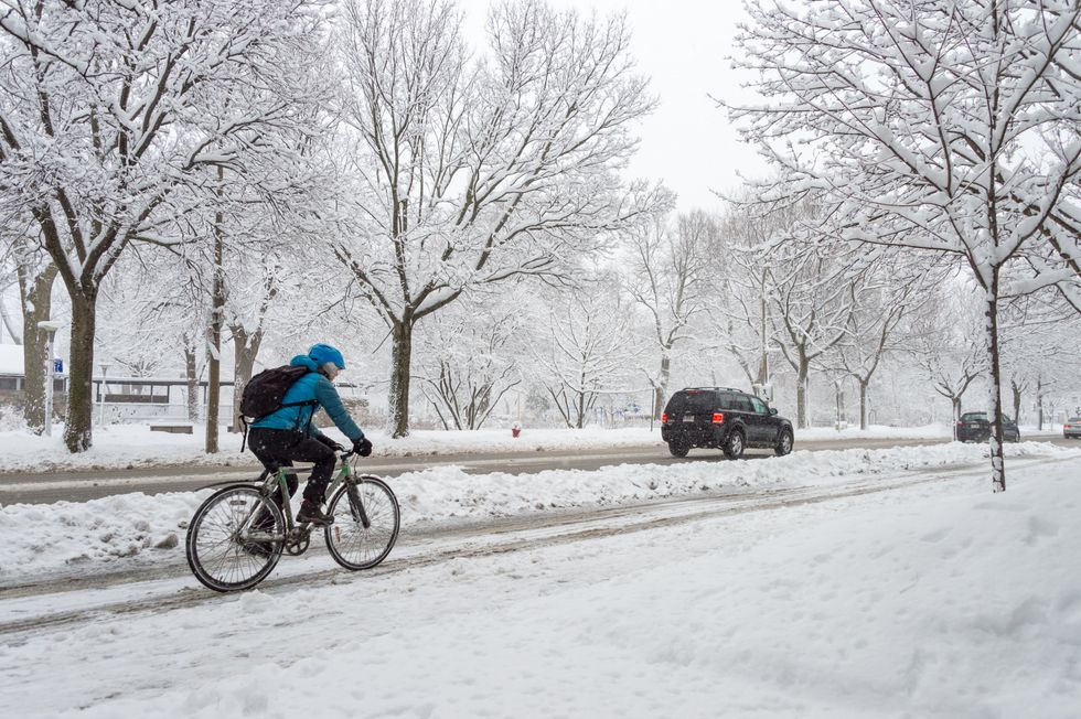 A Montrealer bikes in the winter on a road behind cars.