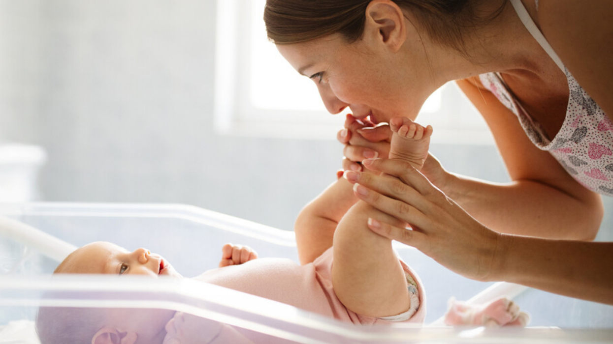 A mother kisses her newborn baby's feet, as the baby lies in a hospital bassinet.