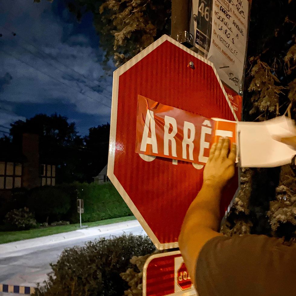 A Nouvelle Alliance membre covering a "STOP" sign with an "ARR\u00caT" sticker.