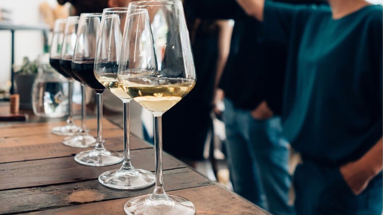 A number of red and white wine in long stem glasses with people tasting wine in the background.