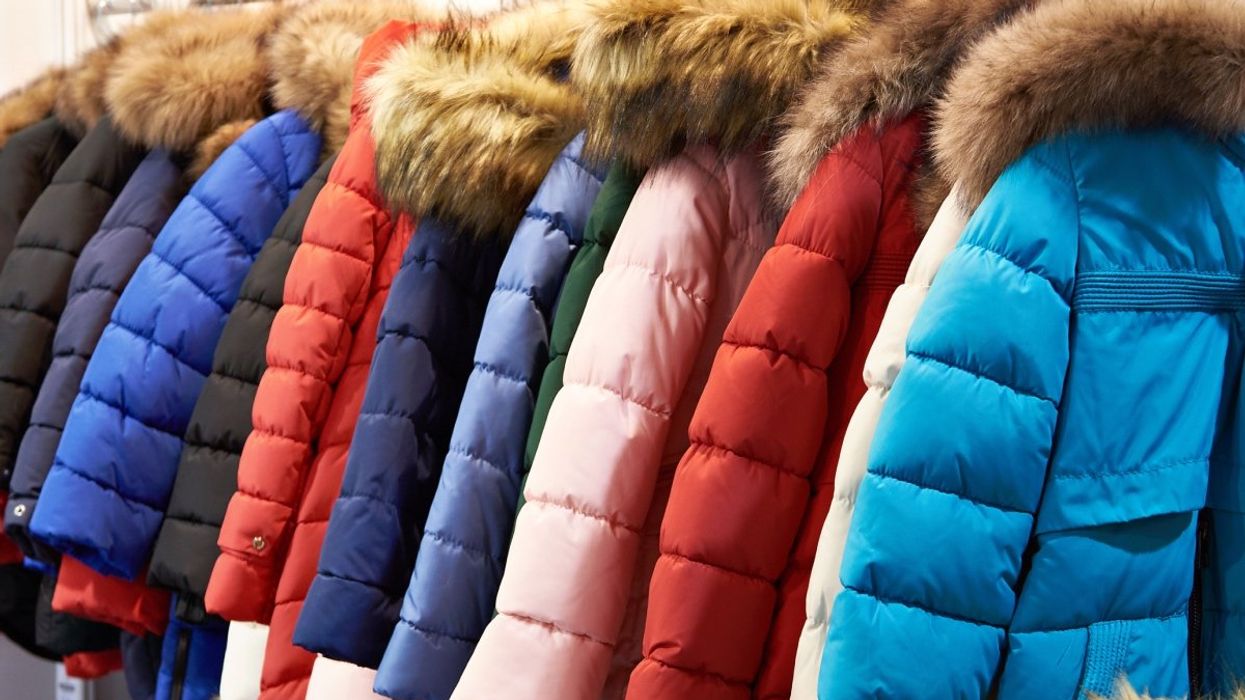 A number of winter jackets with faux fur hoods lined up on a clothing rack.