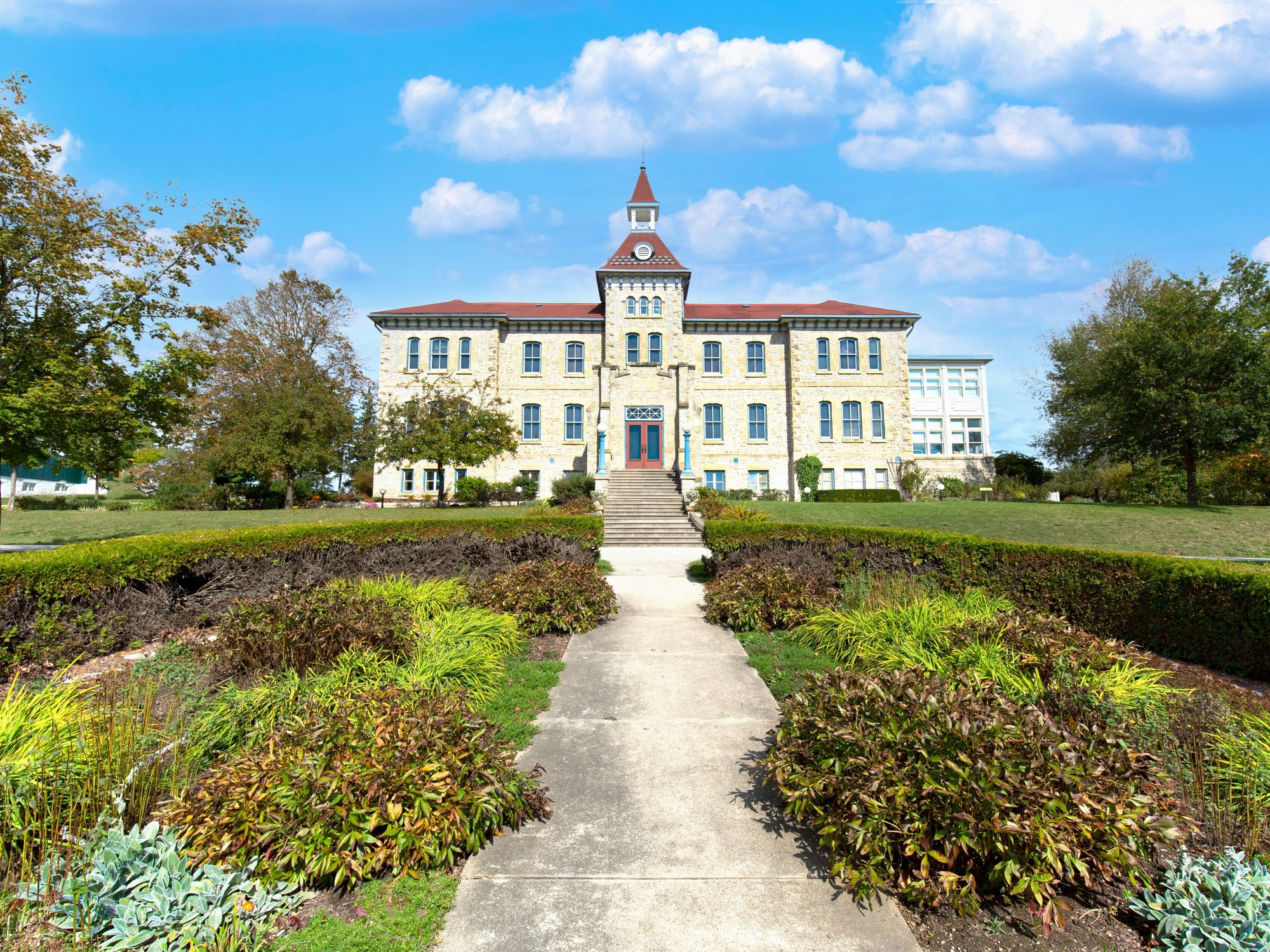 A path leads to a Victorian style building surrounded by trees.