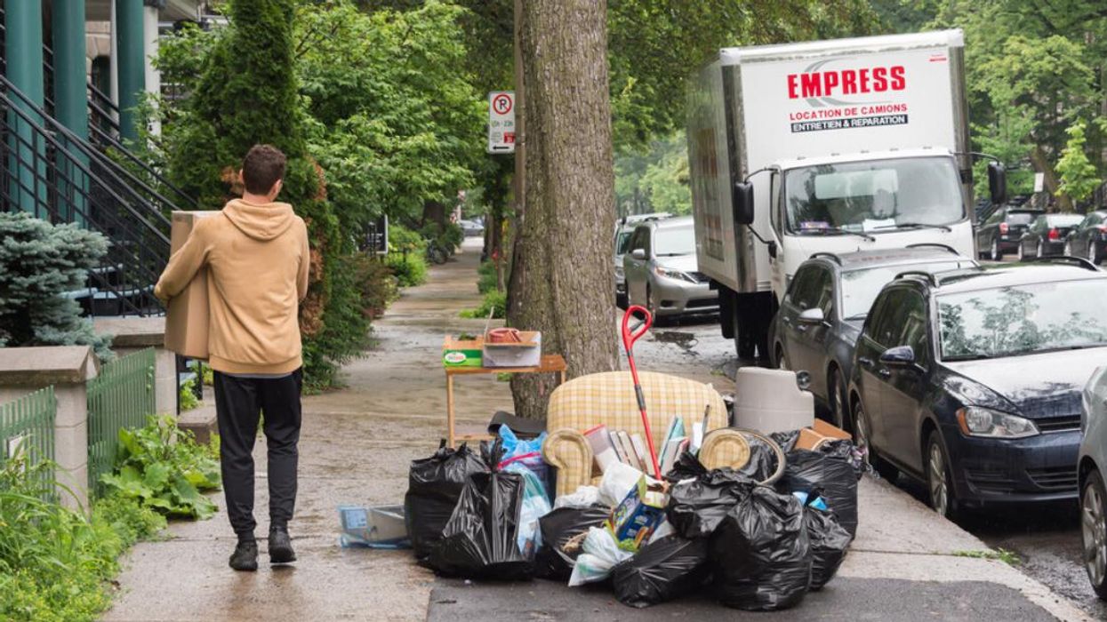 A person carries a box toward a home, next to discarded furniture by the side of the road.