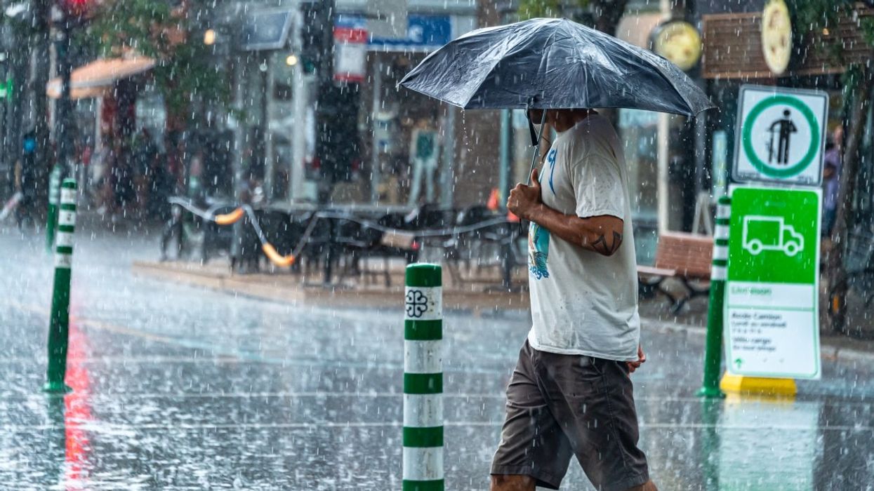 A person crossing a Montreal street during a downpour while holding a half broken umbrella. 