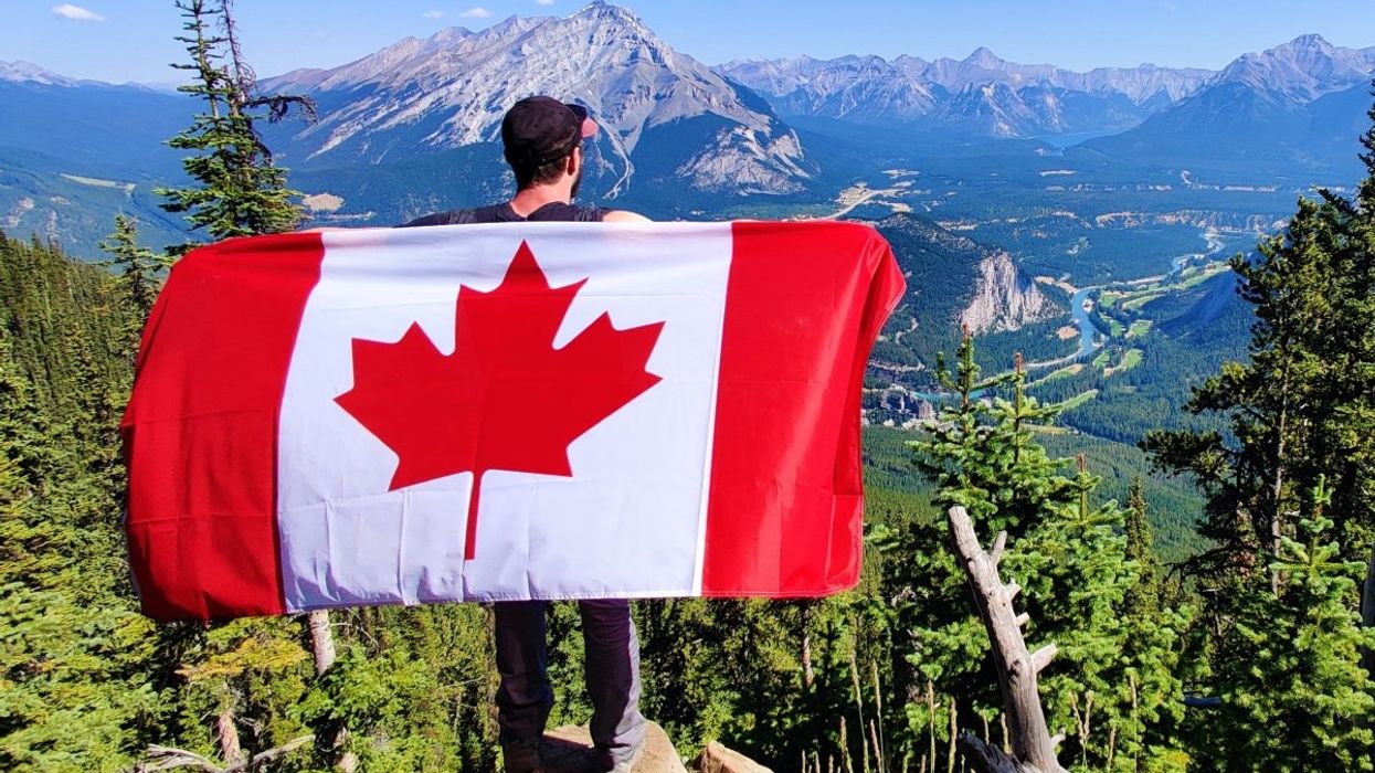 A person holding a Canadian flag overlooking the Canadian Rockies at Banff National Park.