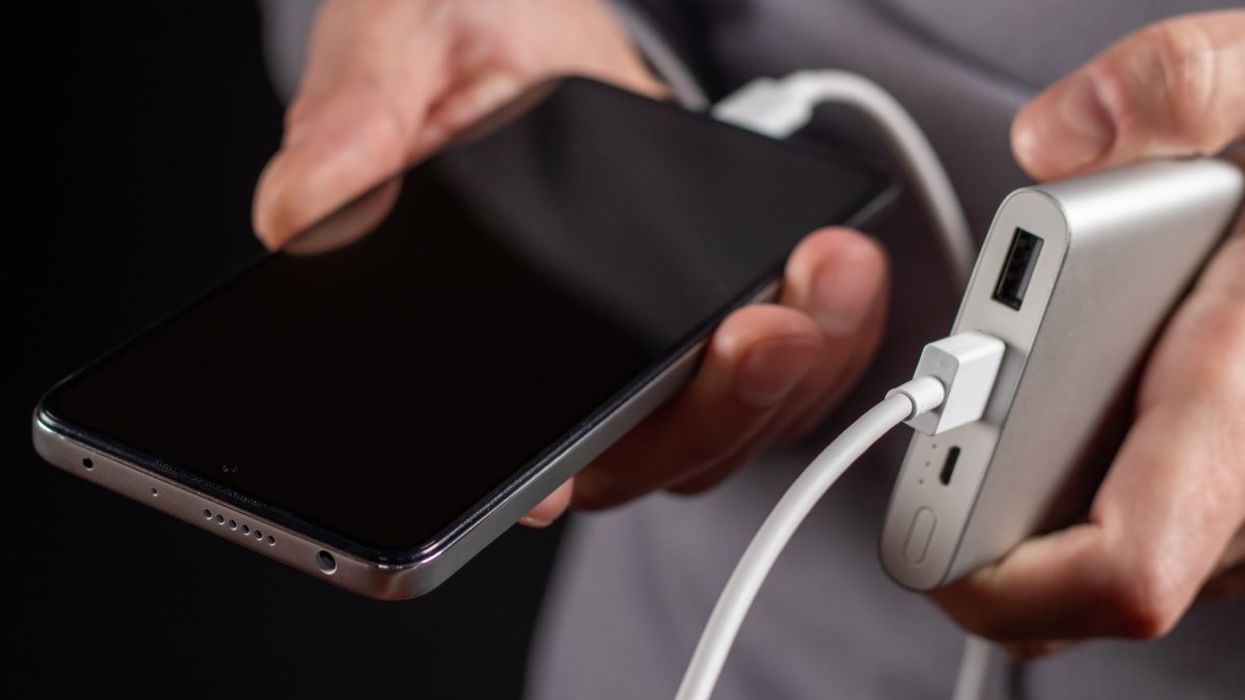 A person holding a smartphone plugged into a portable USB charger battery pack.