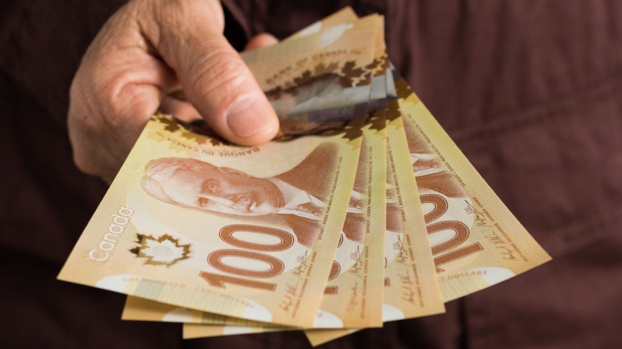 A person holding a stack of four Canadian $100 bills. 