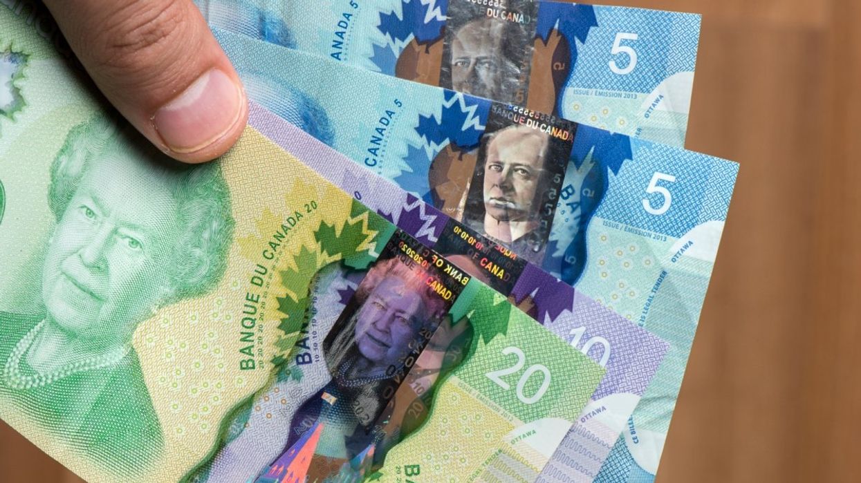 A person holding several Canadian banknotes including a $20 bill, a $10 bill and two $5 bills.