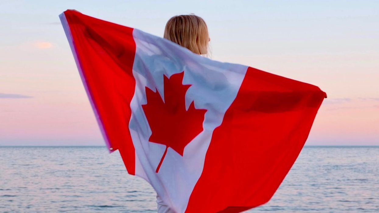 A person holding up a Canadian flag as they look out into a body of water.