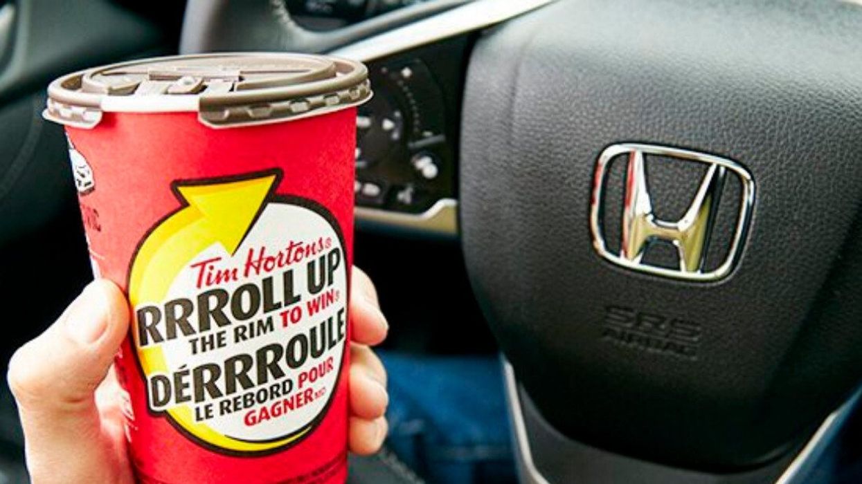A person holds a Tim Hortons coffee cup in their car.