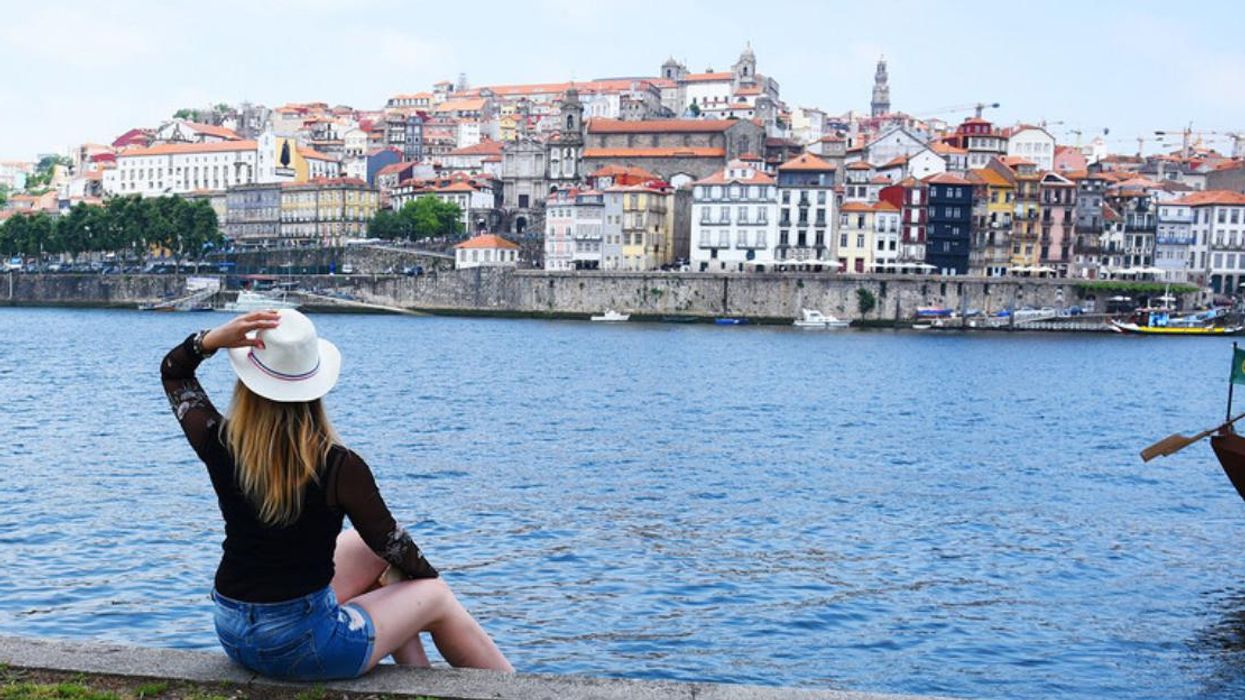 A person holds their hat while sitting by the water in Porto, Portugal.