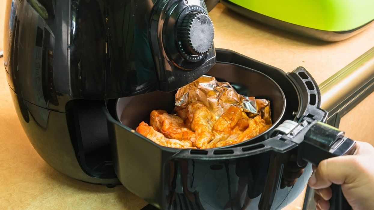 A person pulling out food from an air fryer.