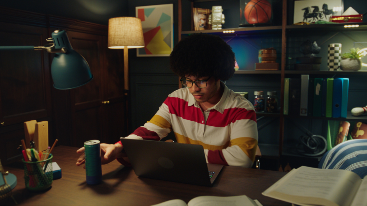 A person reaches for an energy drink while working at a computer late at night.